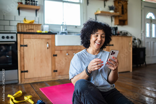 Mature woman smiling at smartphone after workout in home kitchen