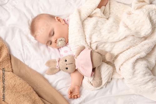 Cute sleeping little baby with pacifier and bunny toy on bed at home