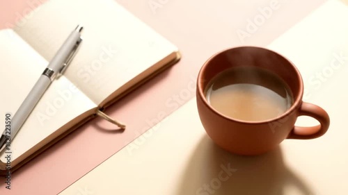 Open notebook with a pen and a steaming cup of hot coffee on a calm desk