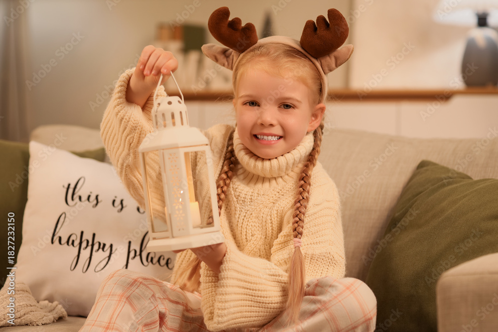 Fototapeta premium Cute little girl with Christmas lantern sitting on sofa at home