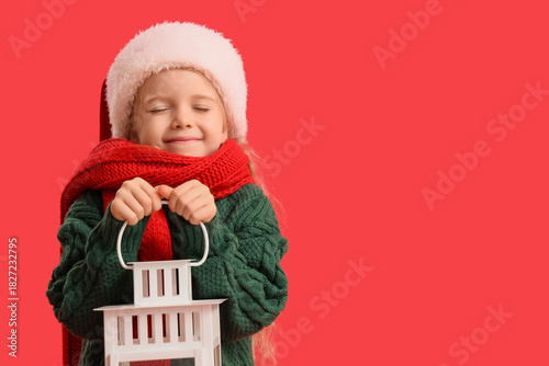 Cute little girl with Christmas lantern on red background