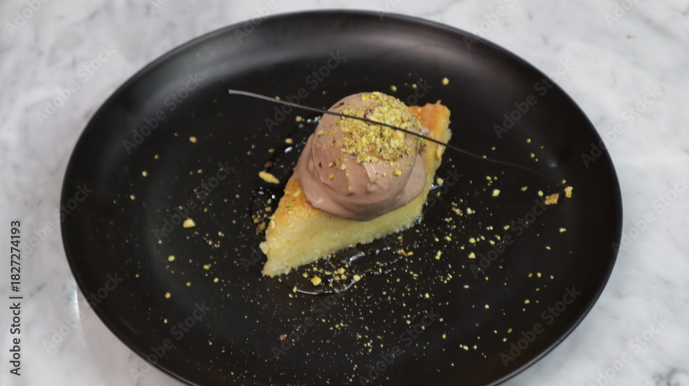 Φωτογραφία Elegant dessert featuring a slice of moist pistachio cake topped with creamy chocolate ice cream, garnished with crushed nuts and served on a black plate