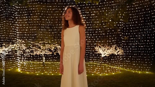 Girl in White Dress Standing Amidst Twinkling Lights at Night
