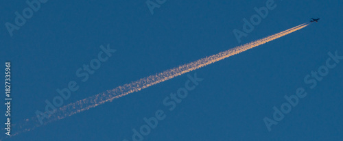 A jet streaking across a deep blue sky trailing pink contrails