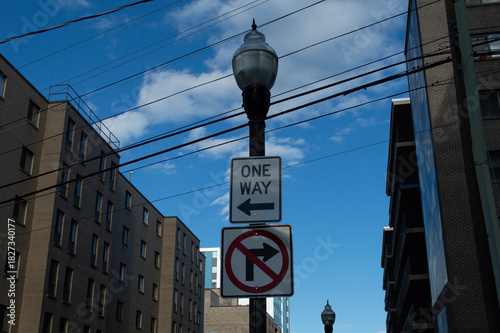 Φωτογραφία Black Lamppost with One Way Arrow and No Right Turn Traffic Signs Against a Blue Sky and Urban Brick Buildings