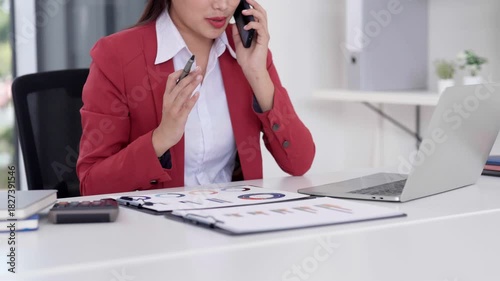 Asian adult businesswoman using smartphone discussing work projects managing business tasks analyzing data with laptop in modern office environment