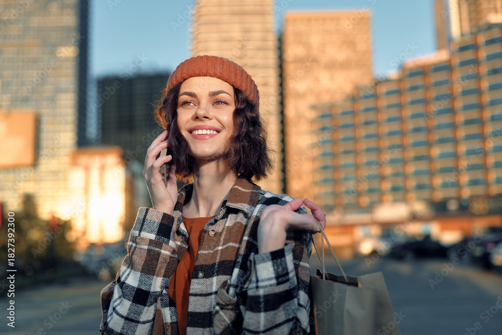Fototapeta premium Woman on phone with shopping bags, smile framed against urban city skyline at golden hour, candid lifestyle portrait conveying authenticity, mindful living and emotional storytelling.