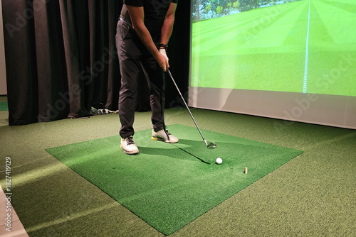 Fototapeta Golfer practicing swing indoors using simulation technology in training setup concept