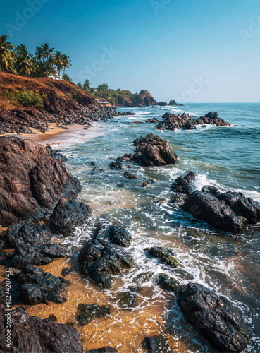 Rocky Coast of Goa or Kerala Beach with Black Rocks and Sand Under Clear Blue Sky.
