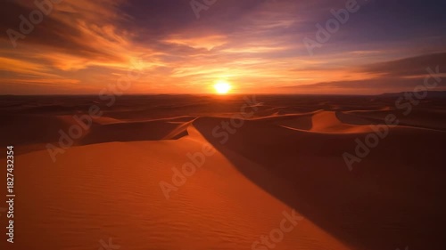 Golden sunset over the Sahara desert dunes creates a scenic orange sky across the arid Moroccan landscape