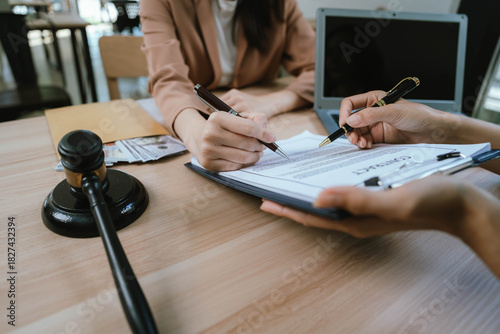 Two professional women discussing legal documents at an office desk, reviewing contracts with a laptop and gavel nearby.