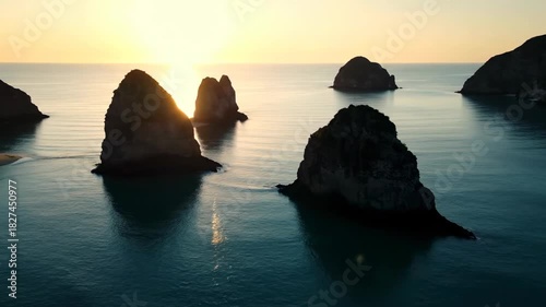 Beautiful sunset landscape over the ocean horizon with orange clouds reflecting on the beach shore and coastal rocks during summer evening dusk