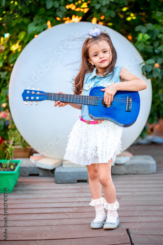 Schilderij op canvas A little girl of European appearance plays the guitar on an impromptu stage, fantasizes that she is a musician