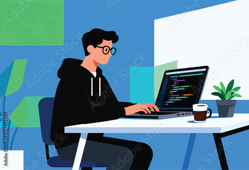 A person in a black hoodie and glasses codes on a laptop at a desk with a coffee mug and plant