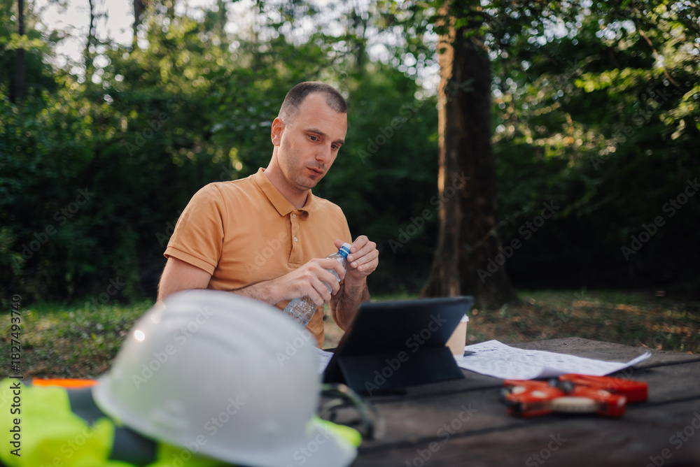 Obraz premium Surveyor opening water bottle while working with tablet in park