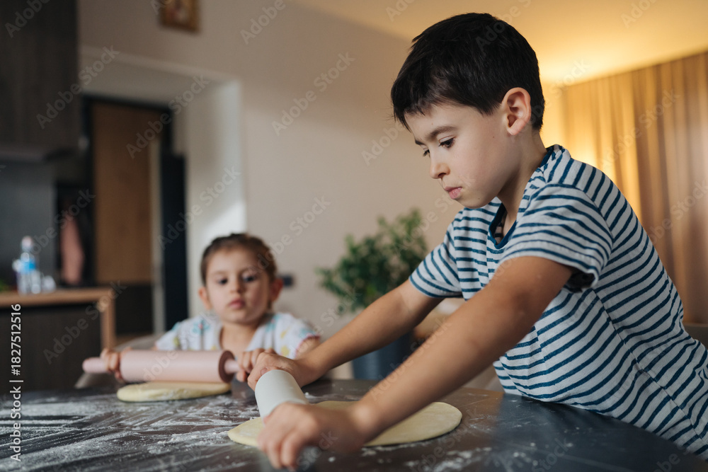 Fototapeta premium young boy carefully concentrates on baking alongside his brother or sister in tranquil kitchen atmosphere
