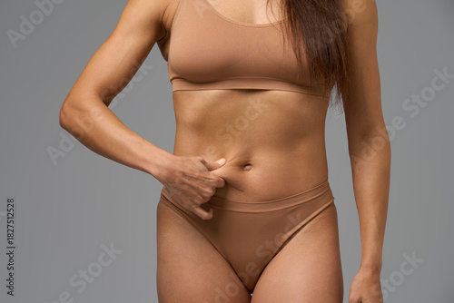 Fit woman in beige underwear pinching her belly skin showing body composition