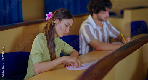 Indian young adult gen z busy pupil boy girl guys sitting on desk table hold pencil do study work exam notes class room. Smart male man female learn new task project day time inside college place