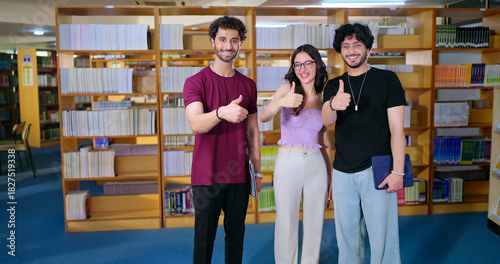 Indian happy young adult gen z male man group standing indoor library look camera spend break time Asian boy girl great team show thumbs up hand sign staring cam do casual pose enjoy fun joy day