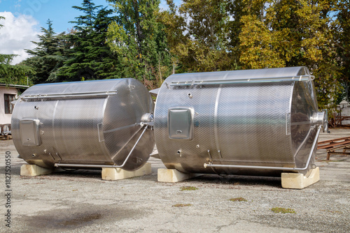 Shiny steel wine production tanks lying on the asphalt on a clear sunny day. Winemaking viticulture wine blend.