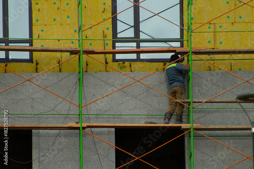 Construction Worker Standing on Scaffolding Applying Cladding to Building Facade