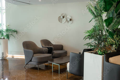 Tableau sur toile Modern interior of a lounge area with two gray armchairs, a glass table, and decorative plants in white pots