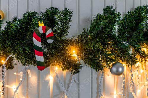 A festive garland decorated with a striped candy cane, silver ornaments, and warm white lights against a wooden background.