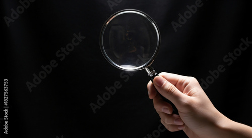 Hand holding magnifying glass against black background for searching and investigating