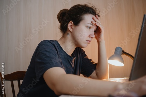 A young woman thinks deeply while working on her laptop, capturing authentic remote work moments. Perfect for modern lifestyle, freelance, and digital nomad concepts