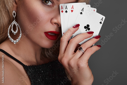 Blonde lady woman in black shiny dress and expensive diamond jewelry is winner money from Omaha Holdem. She is smiling, showing Aces cards to the camera. Ideal style for Poker, Casino, Gambling