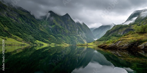Green mountains reflected in crystal-clear fjord waters, moody low clouds in the background