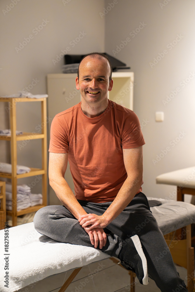 Fototapeta premium Man smiling while receiving a leg stretch from a physical therapist on a table in a clinic, focusing on rehabilitation and health