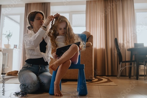 A mother gently brushes her 4-year-old daughter's long beautiful hair. Authentic moment of family hair care, bonding and natural parenting love