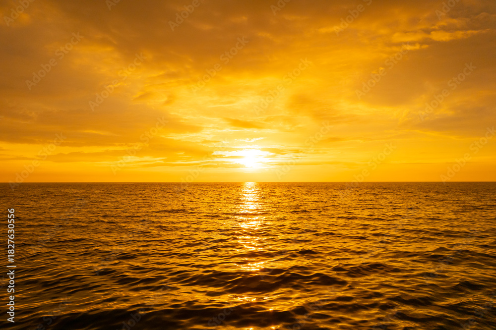 Obraz premium Nature sky breathtaking golden sunset over a calm ocean, with the entire sky and water bathed in brilliant shades of yellow and orange. Streaky clouds enhance the dramatic display of light 