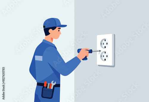 A blue-suited electrician repairs an electrical outlet with a screwdriver, standing against a neutral gray wall