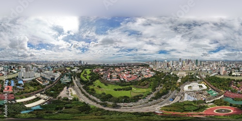 High altitude 360 aerial panorama of Intramuros historic district in Manila, Philippines, with golf course, green parks, Pasig River and city skyline under dramatic cloudy sky.