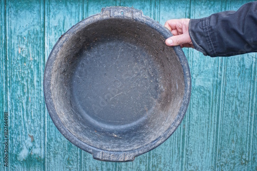 hand holding one black dirty old round plastic basin against green wall background on rural street