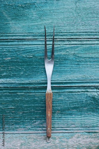 one long large gray metal fork with a brown handle lies on a green wooden table
