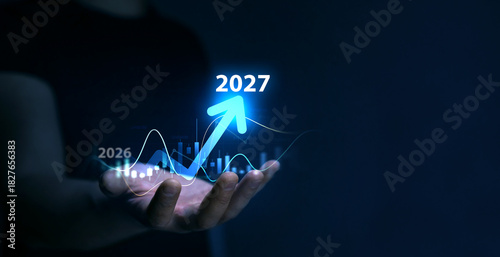 Business plan for increase in 2027 year.Development to success and motivation in new year 2027. Business person draws increase arrow graph corporate future growth year 2026 to 2027. 
