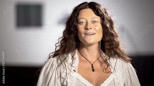Smiling Woman with Long Wavy Hair and White Blouse Looking at Camera.