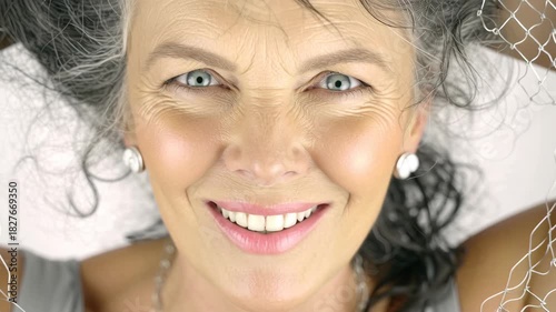 Close-up portrait of a happy senior woman with grey hair smiling directly at the camera.