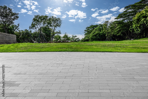 Empty square floor and green grass field with trees under blue sky clouds background.