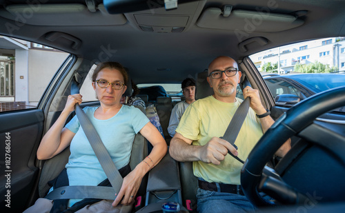 Berlin, Germany 10 August 2023. Car safety concept: a family is sitting in a car, in the foreground a middle-aged husband and wife are fastening their seat belts before driving off