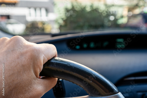 Berlin, Germany, August 10, 2023. Car travel concept: close-up of a hand gripping the steering wheel, blurred background with the car's dashboard and windshield. Travel lifestyle, freedom of movement.