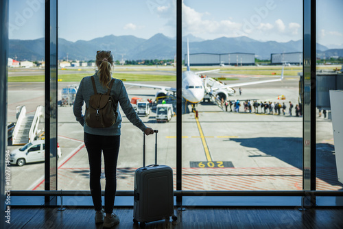 Woman passenger travel with carry-on luggage waiting in airport terminal before boarding to airplane. Solo traveler on her holiday trip