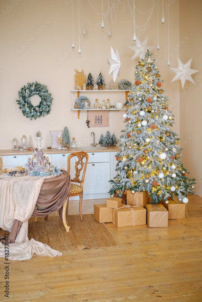 Naklejka premium Elegant decorated Christmas tree with presents and table setting in warm kitchen interior