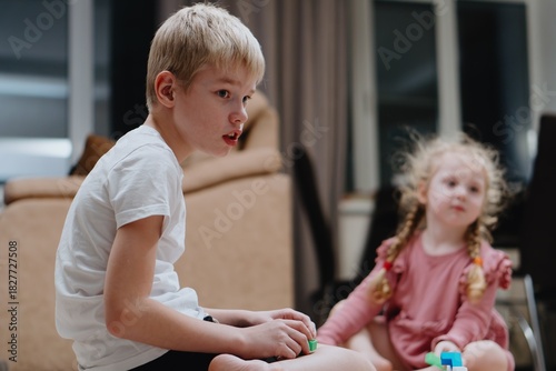 A 9-year-old boy with hearing aids plays naturally with his 4-year-old sister. Authentic sibling bonding moment showcasing inclusive family relationships and childhood joy