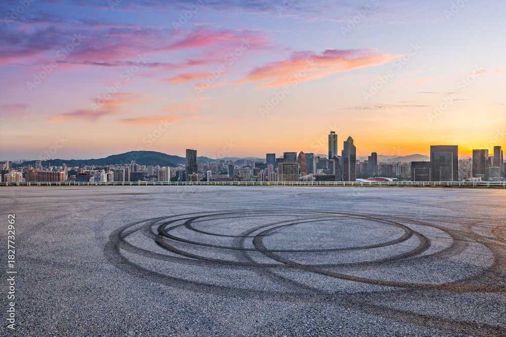 Obraz premium Asphalt road ground with tire tracks and city skyline at sunset