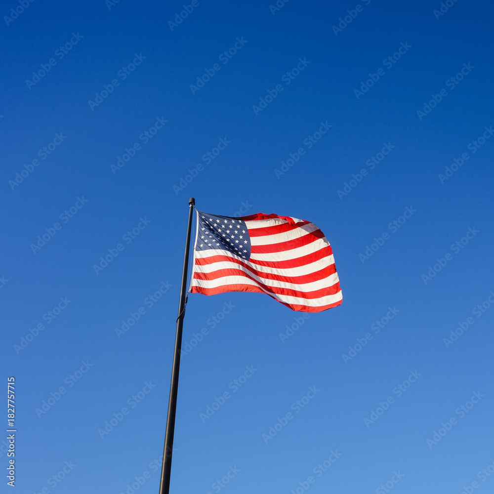 Fototapeta premium Square image of nAmerican flag, also called Stars and Stripes, Old Glory or Star-Spangled Banner flying in blue sky in Maine, USA, symbol for freedom and patriotism, 4th of July