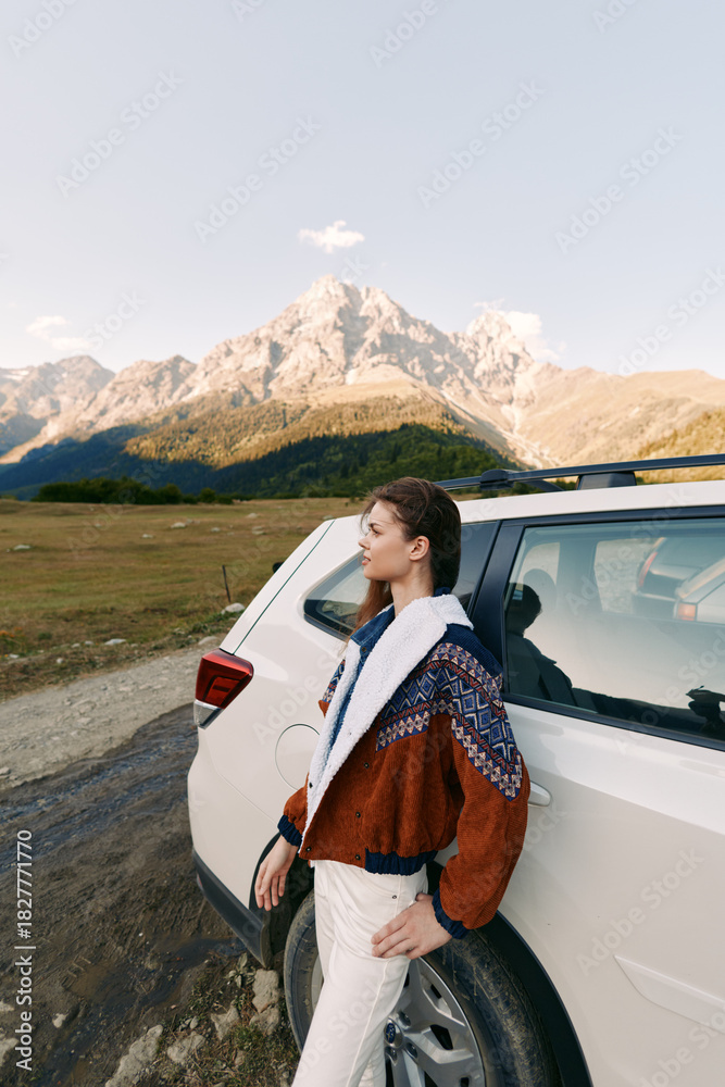 Obraz premium Woman, car, mountains, travel, road, nature: Young woman leaning on a white SUV at the roadside with panoramic alpine peaks, cozy jacket, contemplative pose and outdoor adventure mood.